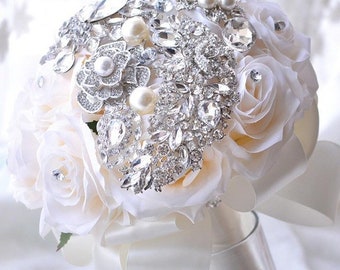 May include: A bridal bouquet made of white silk roses and adorned with a large silver brooch featuring rhinestones and pearls.