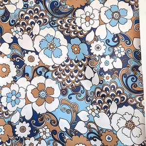 May include: A roll of retro floral wallpaper with a repeating pattern of large white, pale blue, and brown flowers on a dark blue backdrop. The wallpaper is rolled around a brown cardboard tube.