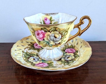 Xícara de chá com pires perfurado em porcelana esterlina com detalhes dourados e rosas, estilo lustroso, amarela com etiquetas.