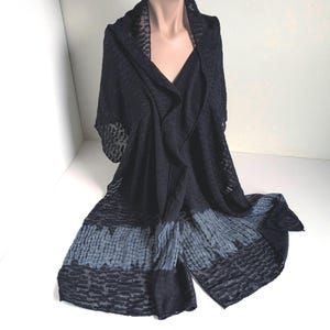 May include: A black shawl draped over a mannequin. The shawl has a textured pattern and a gradient of dark to light gray at the bottom. The fabric appears sheer in areas.