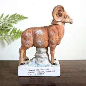 May include: A ceramic ram figurine with a brown body, large curved horns, and black hooves. The ram stands on a white base with the text "CREATED FOR THE FOSS COMPANY, GOLDEN, COLORADO LIMITED EDITION."