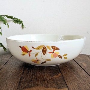 May include: A round, off-white ceramic bowl featuring a decorative floral pattern in shades of yellow, orange, and brown. The bowl has a smooth, curved rim and a wide, shallow basin, showcasing a botanical design with leaves and blossoms.