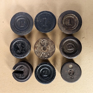 Puede incluir: Nueve pesas de hierro fundido vintage de diferentes tamaños, incluyendo pesas de 1 lb y 4 lb. Las pesas son redondas y tienen un acabado negro. Algunas pesas tienen un número en relieve en la parte superior, mientras que otras tienen un diseño en relieve.