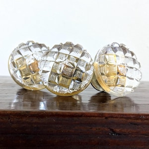 May include: Three round cabinet knobs made of clear glass with a faceted, diamond-cut geometric pattern. Each knob features a reflective surface that catches light, creating a grid-like texture across the circular face of the hardware pieces.