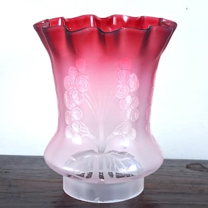 Puede incluir: Una pantalla de lámpara de vidrio con un borde superior ondulado y un degradado de color que va desde el rojo intenso en el borde hasta una base de vidrio esmerilado. La superficie exterior presenta un patrón floral grabado de flores.
