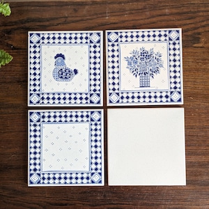 Puede incluir: Cuatro baldosas de cerámica cuadradas con diseños azules y blancos. Tres baldosas presentan un borde de diamantes azules y blancos, con un diseño central de una gallina, un arreglo floral y un patrón de puntos. La cuarta baldosa es blanca lisa.