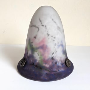May include: A vintage glass lampshade with a bell shape. The shade features a gradient of colors, including purple, pink, and green, with a frosted white top. Two decorative metal accents are on the base. This lampshade is a unique home decor item.