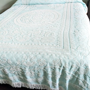 Peut inclure: Un couvre-lit bleu clair orné d'un motif floral touffeté blanc en relief et d'un médaillon circulaire central. Le textile présente une surface texturée à rayures verticales et est fini avec une frange blanche décorative sur le bord inférieur.