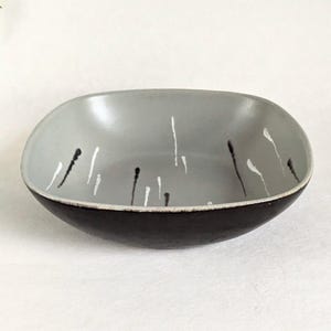 May include: A shallow, square-shaped bowl with rounded corners. The exterior is a solid dark brown, while the interior is a light gray featuring vertical, thin, hand-painted drip patterns in alternating black and white paint strokes.