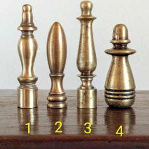 Pode incluir: Quatro terminais de lat&atilde;o antigo de v&aacute;rias formas e tamanhos. Os terminais s&atilde;o numerados de 1 a 4. Os terminais s&atilde;o exibidos em uma superf&iacute;cie de madeira escura. Os terminais s&atilde;o feitos de lat&atilde;o e t&ecirc;m um tom dourado quente.