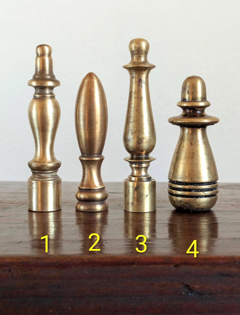 Pode incluir: Quatro terminais de lat&atilde;o antigo de v&aacute;rias formas e tamanhos. Os terminais s&atilde;o numerados de 1 a 4. Os terminais s&atilde;o exibidos em uma superf&iacute;cie de madeira escura. Os terminais s&atilde;o feitos de lat&atilde;o e t&ecirc;m um tom dourado quente.