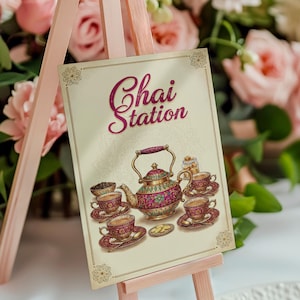 May include: A decorative sign on a pink easel with the words "Chai Station" in a cursive font. The sign features an illustration of a teapot, teacups, and snacks in shades of red, gold, and green.
