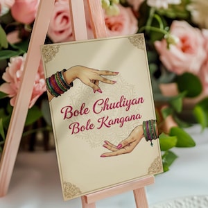 Op de afbeelding: Een rechthoekig bord op een roze ezel toont de tekst "Bole Chudiyan Bole Kangana" in bordeauxrood schrift. Het bord heeft illustraties van handen met kleurrijke armbanden. De achtergrond bevat een bloemenontwerp en roze rozen.