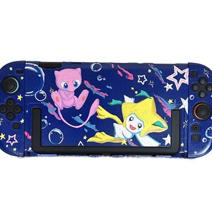 May include: A navy blue Nintendo Switch console case featuring a vibrant design with cartoon characters Mew and Jirachi. The case is adorned with stars, bubbles, and colorful accents, creating a playful and eye-catching aesthetic.