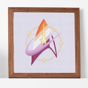 May include: A framed cross-stitch of a Starfleet insignia. The design incorporates orange, yellow, pink, and purple colours. The artwork is set within a wooden frame, adding a traditional feel to this handmade item.