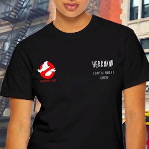May include: Black t-shirt with a white ghostbuster logo and the text "Herrmann Containment Crew" printed on the front.