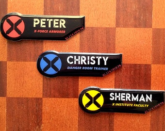 May include: Three black rectangular name badges with rounded ends featuring a circular X logo. The top badge reads PETER X-FORCE ARMORER, the middle reads CHRISTY DANGER ROOM TRAINER, and the bottom reads SHERMAN X INSTITUTE FACULTY, all with code XL.114.1010.78.