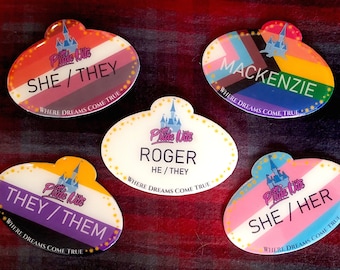 May include: Five oval-shaped name tags with a castle graphic and the text "Pride Nite" in a pink script font. Each tag features a different pride flag and the text "Where Dreams Come True". The name tags include the names "Mackenzie", "Roger", and pronouns such as "She/They", "He/They", "They/Them", and "She/Her".