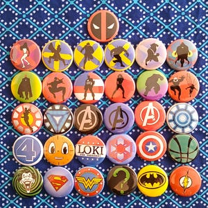 May include: A collection of 25 round buttons featuring various Marvel characters and logos. The buttons are colourful and have a glossy finish. Some of the characters featured include Iron Man, Captain America, Thor, Hulk, Black Widow, Hawkeye, and Loki. The buttons also feature logos such as the Avengers logo, the Shield logo, and the Star Wars logo.