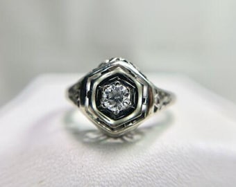 May include: A silver ring with a delicate filigree design and a single round diamond in the center.