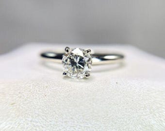 May include: A silver solitaire engagement ring with a round brilliant cut diamond.