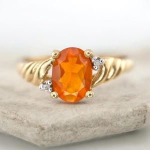 Peut inclure: Une bague en or ornée d'une pierre précieuse orange ovale et de petits diamants. La bague a un design de bande torsadée. La pierre précieuse est le point central, sertie dans un sertissage à quatre griffes.