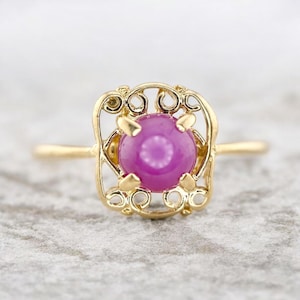 Peut inclure: Une bague en or ornée d'une grosse pierre précieuse magenta ronde. La pierre est sertie dans un cadre ajouré décoratif avec des détails de filigrane tourbillonnants. L'anneau est en or poli.