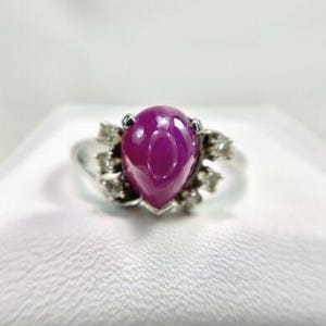May include: A pear-shaped ruby ring set in white gold with a halo of small diamonds.