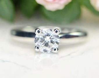 May include: A silver engagement ring with a round, clear diamond.