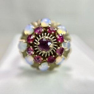May include: A gold ring with a cluster of pink and white gemstones. The center stone is a larger pink gemstone surrounded by smaller pink and white gemstones.