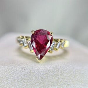 May include: A pear-shaped ruby gemstone ring set in yellow gold with baguette-cut diamonds on the band.