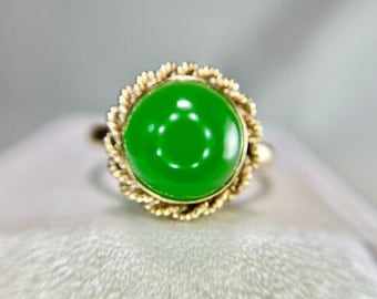 Könnte beinhalten: Ein goldener Ring mit einem grünen Jade-Stein, der in einem seilartigen Design gefasst ist.