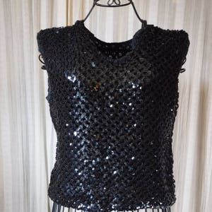 May include: A sleeveless black sequined top with a round neckline. The top is made of a soft, stretchy fabric and is perfect for a night out.