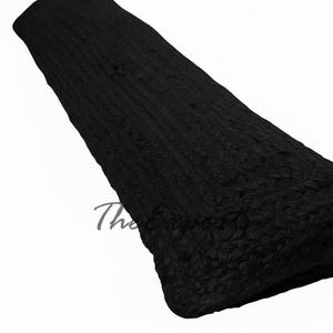 May include: A folded, black woven rug with a textured surface. The rug is rectangular and appears to be made of a thick, durable material. The rug is against a white background.