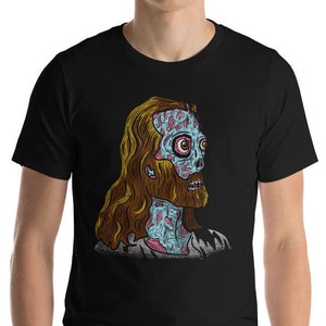Puede incluir: Una camiseta negra con un gráfico de un Jesús zombie. El Jesús zombie tiene la piel azul, venas rosadas y rojas y cabello castaño. El gráfico está en el centro de la camiseta.