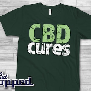 May include: A dark green t-shirt with the text "CBD cures" in white and green letters with a distressed look.
