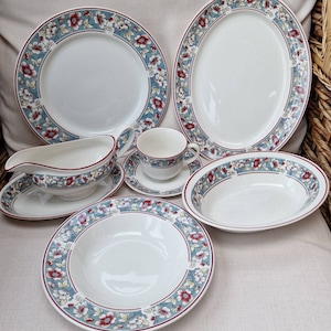 May include: A set of white ceramic dishes with a blue and red floral pattern. The set includes a large oval platter, a smaller round plate, a bowl, a gravy boat, and a teacup and saucer.