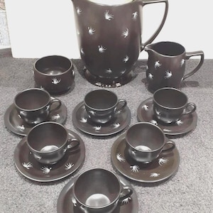 Op de afbeelding: Een zwart-wit theeservies met een bloemenmotief. De set bevat een theepot, een roomkan, een suikerpot en zes kopjes en schoteltjes.