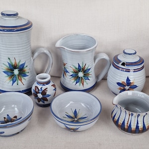 Puede incluir: Conjunto de seis piezas de cerámica con un esmalte blanco y diseños florales azules, verdes y marrones. El conjunto incluye una jarra, una jarra de crema, un azucarero, un jarrón y dos cuencos.