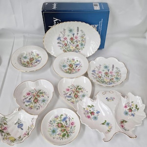 May include: Aynsley fine bone china tableware set featuring a floral design. The collection includes an oval serving platter, bowls, and decorative dishes in various shapes, all with gold edging. The floral pattern showcases a mix of colorful flowers.
