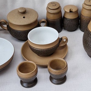 Puede incluir: Un juego de vajilla de cerámica marrón y blanca, que incluye una tetera, una jarra de crema, un azucarero, tazas y platillos. Las piezas tienen un acabado texturizado y moteado.