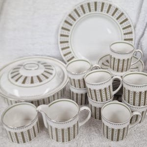 May include: A complete vintage dinnerware set featuring white and olive green accents. The set includes plates, cups, saucers, a serving dish with a lid, and a creamer. The pieces have a repeating vertical stripe pattern and silver trim.