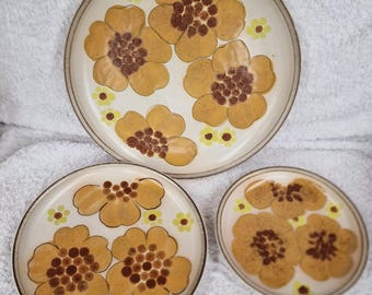 May include: Set of three ceramic plates with a floral design. The plates are white with brown and yellow flowers. The largest plate is 25 cm in diameter, the medium plate is 20 cm in diameter, and the smallest plate is 15 cm in diameter.