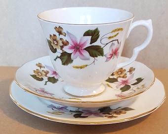 May include: A white teacup and saucer set with a floral pattern. The teacup has a gold rim and the saucer has a gold band around the edge. The floral pattern features pink, yellow, and green flowers.