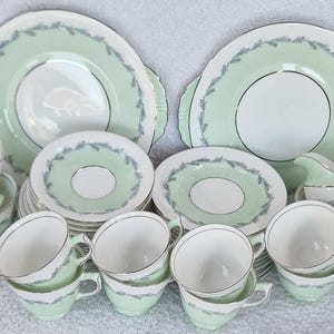 Può includere: Un set di tazze da tè e piattini in porcellana verde e bianca con un delicato motivo floreale. Il set comprende una teiera, un bricco per la panna e una zuccheriera.