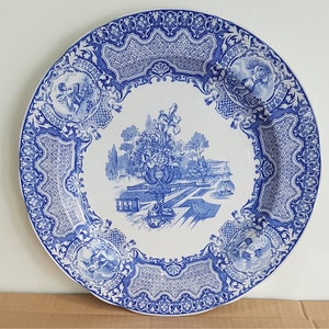 Könnte beinhalten: Ein blauer und weißer Keramikteller mit einem Blumendesign und einer Gartenszene. Der Teller hat einen dekorativen Rand mit einem sich wiederholenden Muster.