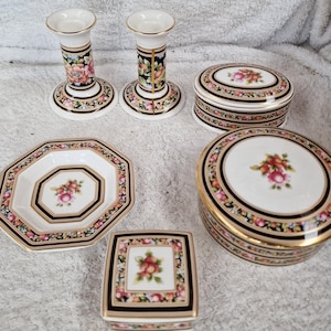Può includere: Una collezione di oggetti decorativi in porcellana con disegni floreali. Include due candelabri, due scatole con coperchio, una piccola scatola quadrata e un piatto ottagonale. I pezzi presentano una base bianca con dettagli neri, dorati e floreali.