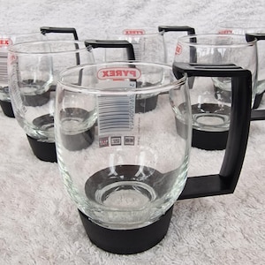 May include: A set of clear glass mugs with black handles and bases. Each mug has a red and white Pyrex label. The mugs are designed for easy handling and are suitable for various beverages. The mugs are made of clear glass.