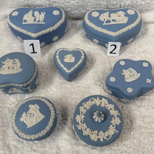 Może przedstawiać: Kolekcja niebiesko-białych ceramicznych pudełek na biżuterię w różnych kształtach, w tym serca, okręgi i kształt kwiatu. Każde pudełko ma biały reliefowy wzór i białą kwiatową lub geometryczną obwódkę. Pudełka są wyświetlane na białej powierzchni.