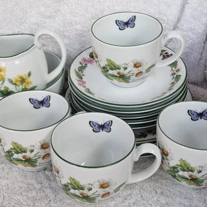 May include: A white porcelain tea set featuring a floral and butterfly design. The set includes cups, saucers, a creamer, and bowls. Each piece has a green trim and a delicate flower and butterfly pattern.